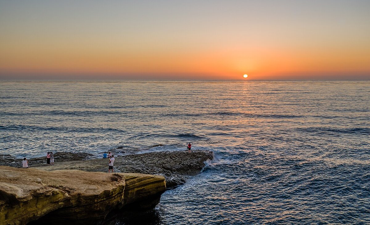 waves crashing against eroded sandstone cliffs at sunset